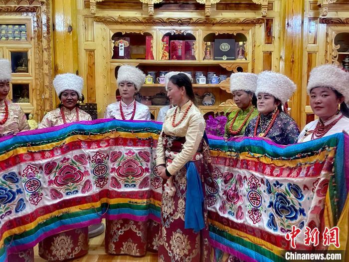圖為女性展示村民自發(fā)繡制的“百米五彩哈達(dá)”?！±钣穹?攝